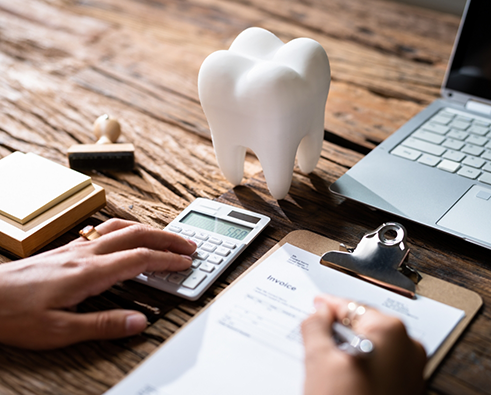 Using calculator and writing on form on clipboard with model tooth sitting nearby
