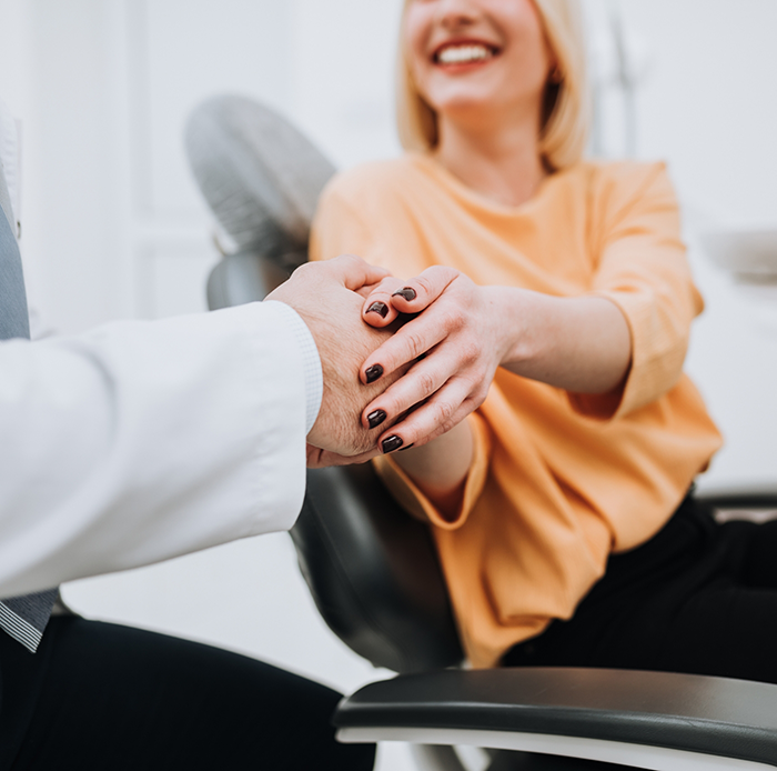Woman in dental chair shaking hand of dentist