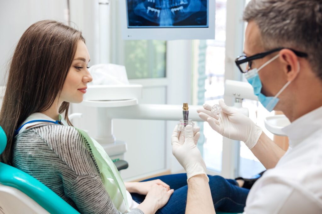 Dentist discussing sample implant with patient in dental chair