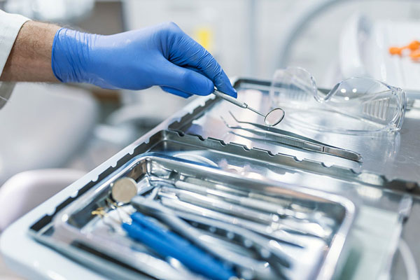 Dental tools on a tray with a gloved hand preparing for a fluoride treatment and teeth cleaning at Kimberley Lane Cosmetic and Family Dentistry.