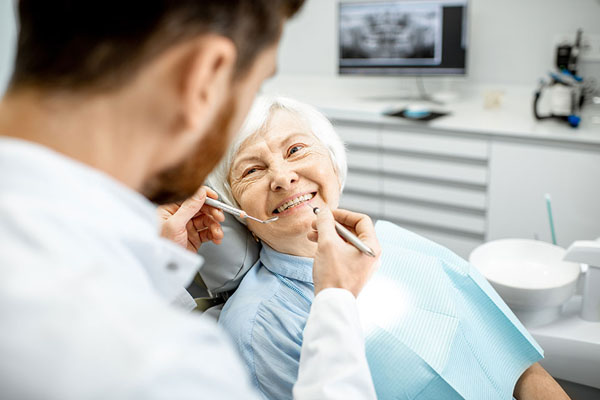 Elderly woman smiling in dental chair during professional teeth cleaning, with dentist using dental instruments in modern clinic setting.