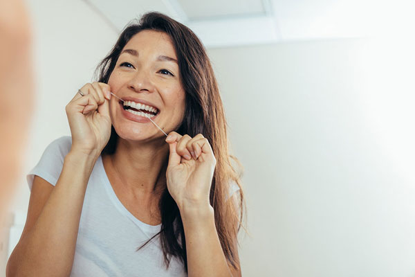 Woman smiling while flossing her teeth, emphasizing daily oral hygiene after fluoride treatments for maintaining dental health.