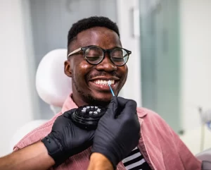 Smiling patient in dental chair receiving shade matching for porcelain veneers during cosmetic dentistry consultation.